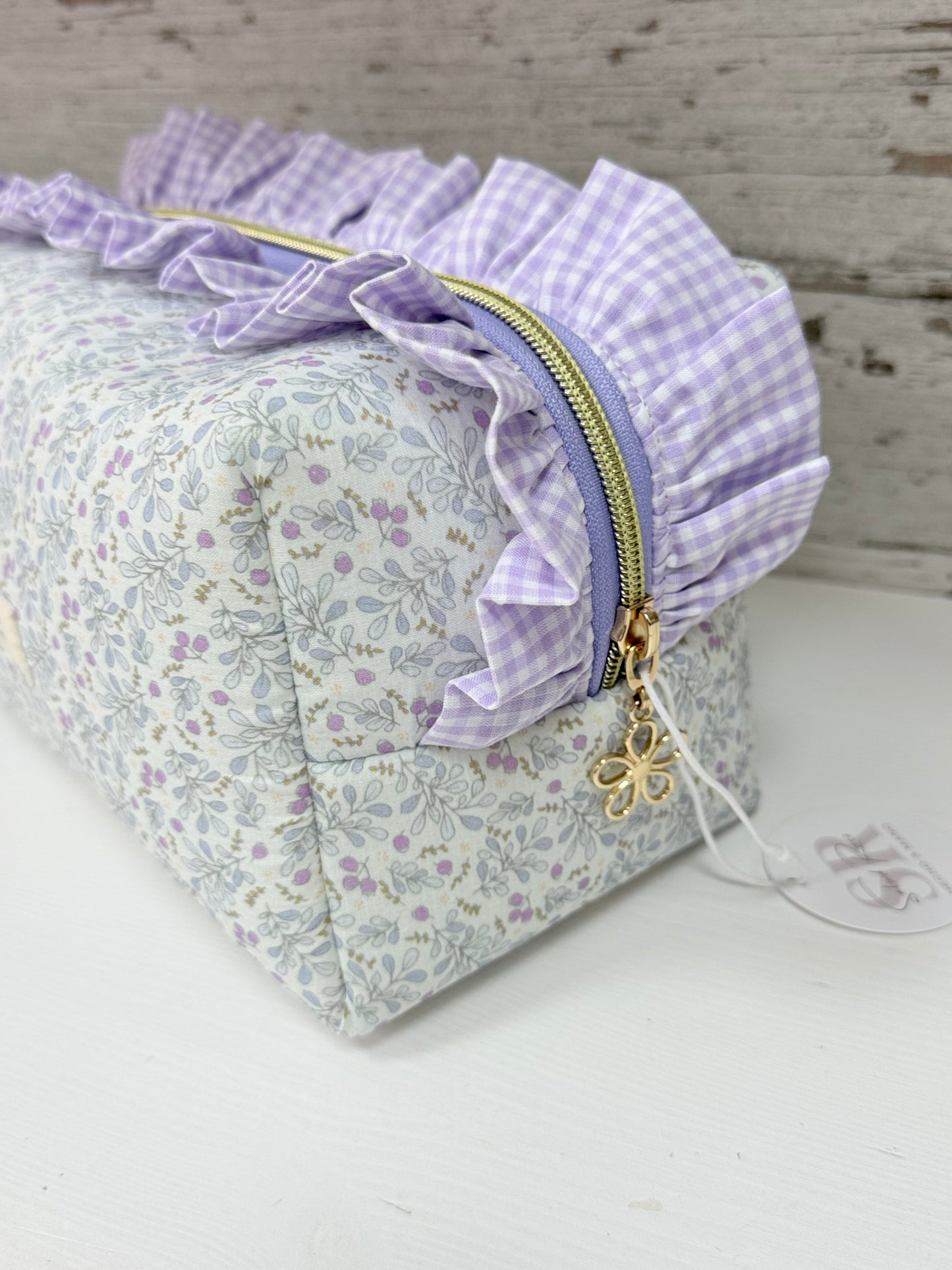 Detalle lateral de neceser de tela cuadrado con volante fruncido vichy, cremallera con tirador de estrella y estampado floral artesanal.