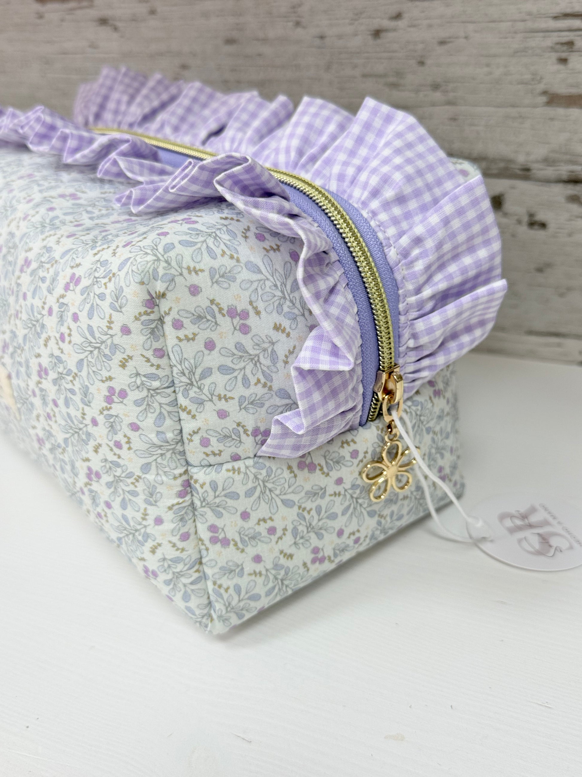 Detalle lateral de neceser de tela cuadrado con volante fruncido vichy, cremallera con tirador de estrella y estampado floral artesanal.