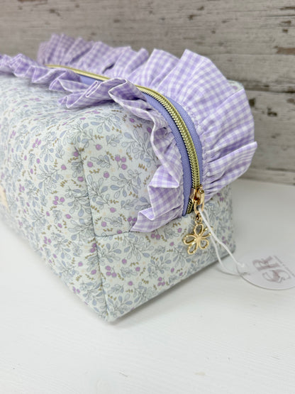 Detalle lateral de neceser de tela cuadrado con volante fruncido vichy, cremallera con tirador de estrella y estampado floral artesanal.